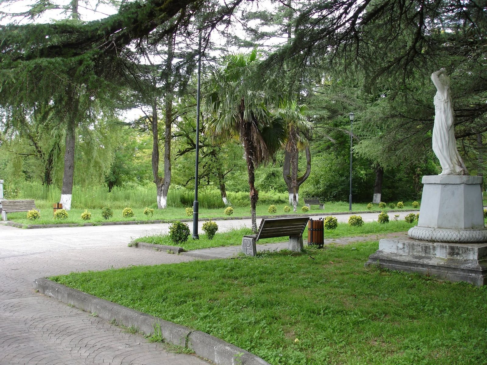 Le parc de la ville : massifs de fleurs, bancs et une statue de marbre au bord de l'allée.