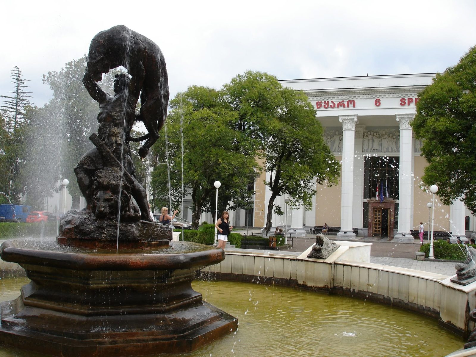 Une fontaine ornée d'une sculpture devant un bâtiment à colonnes.