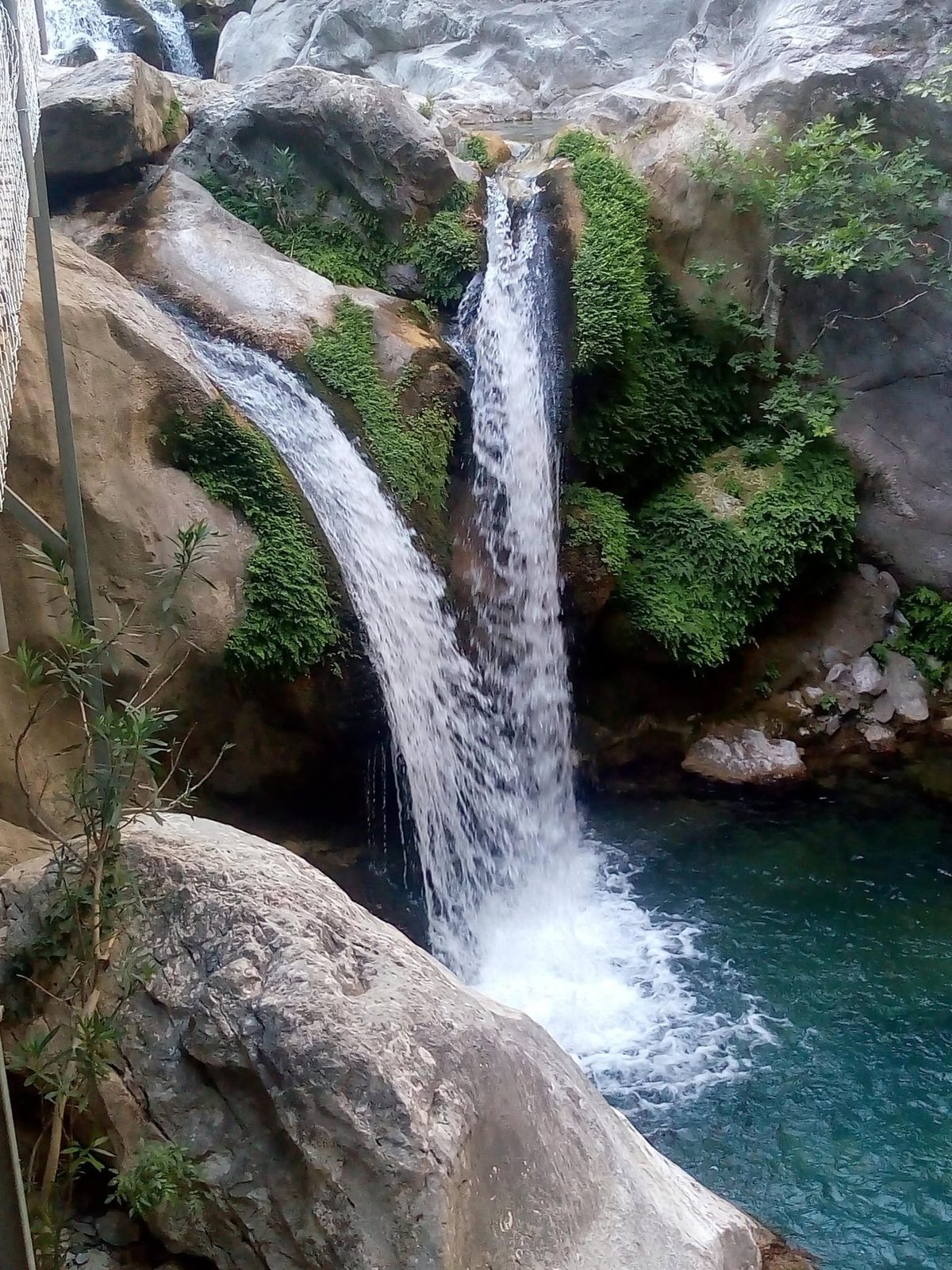 Une cascade tombe dans un bassin turquoise entre des rochers couverts de mousse.