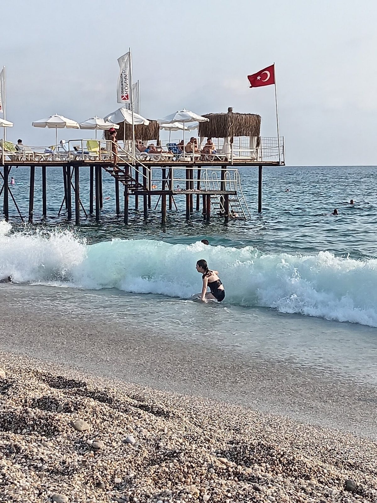 Une plage avec des vagues et une jetée en bois. Un drapeau flotte au mât.